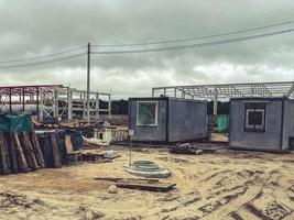 canteiro de obras de um complexo industrial. pequenas casas para construtores com janelas no local da construção da fundação. sujeira na rua, mentiras de material de construção foto