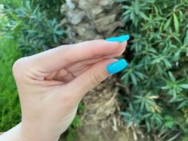 Feche a mão de uma mulher mostrando esmalte azul enquanto segura uma folha. estilo de nail art, beleza, conceito de manicure foto