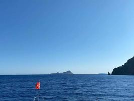 a bandeira turca acenando em um fundo de mar calmo com um barco e céu azul foto