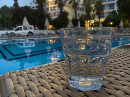 copo com coquetel de laranja em frente a uma piscina com água limpa foto