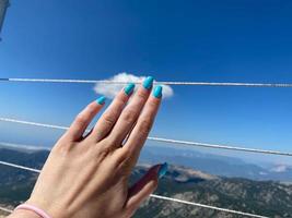 mão feminina com uma linda manicure azul no fundo de uma montanha alta. conceito de beleza, turismo e viagens foto