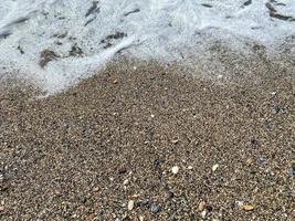 ondas de água no mar e areia com pequenas pedras multicoloridas naturais à beira-mar, pequenas pedras na praia. fundo, textura foto