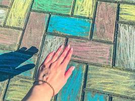 asfalto pintado com giz de cera, textura, plano de fundo. pedras de asfalto são pintadas em cores brilhantes. contra o fundo do asfalto, a mão de uma garota com uma linda manicure rosa foto