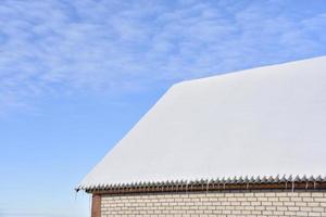 o telhado da casa está na neve branca com um céu azul. o telhado da casa coberto de neve no inverno. uma casa com janelas e neve no telhado. foto