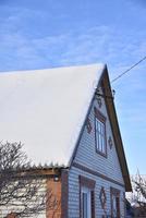 o telhado da casa está na neve branca com um céu azul. o telhado da casa coberto de neve no inverno. uma casa com janelas e neve no telhado. foto