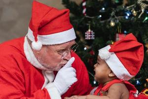 papai noel está silenciando o bebê chorando com a árvore de natal nas costas foto