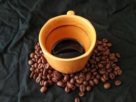 xícara de café e grãos de café em fundo preto foto