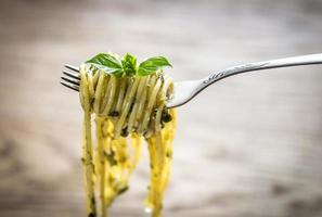 espaguete com molho pesto e folha de manjericão no garfo foto