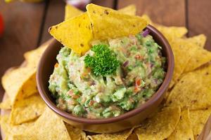 abacate guacamole, limão, tomate, cebola e coentro, servido com nachos - lanche mexicano tradicional foto