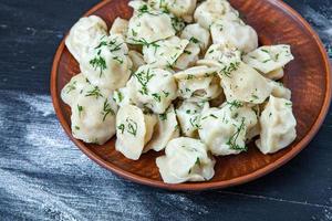 pelmeni russo tradicional ou ravioli, bolinhos com carne em fundo preto de madeira. comida russa e conceito de cozinha russa. foto