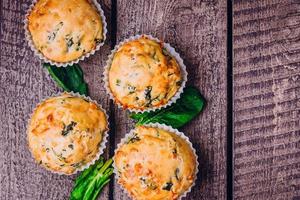 muffins com espinafre e queijo no fundo da mesa de madeira. conceito de comida de café da manhã saudável foto