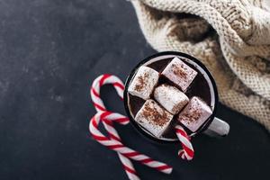 bebida aconchegante de inverno. copo com chocolate quente com marshmallow, pirulito, cachecol aconchegante. vista do topo foto