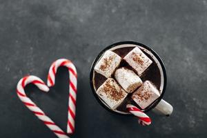 bebida aconchegante de inverno. copo com chocolate quente com marshmallow e pirulito em fundo escuro
