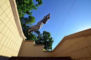 um jovem dá um salto pelo espaço entre os parapeitos de concreto. o atleta pratica parkour, treinando em condições de rua. vista de baixo foto