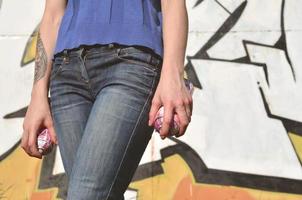foto da mão de uma menina com latas de tinta aerossol nas mãos em um fundo de parede de grafite. o conceito de arte de rua e uso de tintas aerossóis. imagem de fundo da loja de arte graffiti