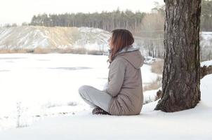 uma jovem caucasiana com um casaco marrom olhando para longe na linha do horizonte entre o céu e o lago congelado no inverno foto