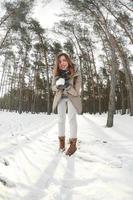 uma jovem e alegre garota caucasiana com um casaco marrom segura uma bola de neve em uma floresta coberta de neve no inverno. foto olho de peixe