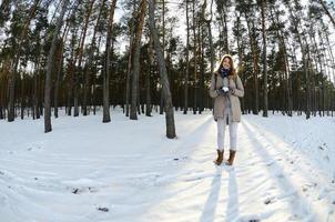 uma jovem e alegre garota caucasiana com um casaco marrom segura uma bola de neve em uma floresta coberta de neve no inverno. foto olho de peixe