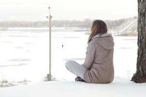 uma jovem caucasiana com um casaco marrom olhando para longe na linha do horizonte entre o céu e o lago congelado no inverno foto