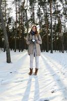 uma jovem e alegre garota caucasiana com um casaco marrom segura uma bola de neve em uma floresta coberta de neve no inverno. foto olho de peixe