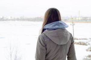 uma jovem caucasiana com um casaco marrom olhando para longe na linha do horizonte entre o céu e o lago congelado no inverno foto