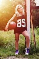 jovem loira com basquete laranja posando ao ar livre foto
