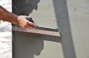 mãos de um velho trabalhador manual com ferramentas de reboco de parede renovando a casa. estucador renovando paredes externas e cantos com espátula e gesso. isolamento de parede. obras de acabamento foto