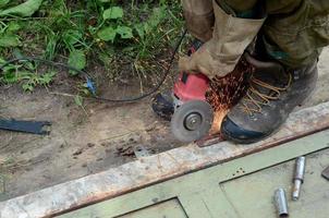 moagem de roda elétrica na estrutura de aço ao ar livre. antigo trabalhador manual em luvas de proteção cortando porta de metal com moedor foto