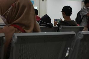 um homem indonésio está sentado em uma cadeira esperando em um hospital jogando em seu smartphone esperando que sua família receba tratamento. foto