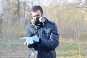retrato de jovem com máscara protetora de gás usa luvas descartáveis de borracha ao ar livre em madeira de primavera foto