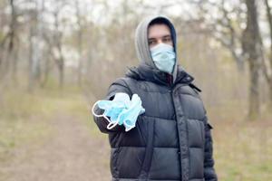 jovem com máscara protetora mostra um monte de máscaras protetoras ao ar livre em madeira de primavera foto