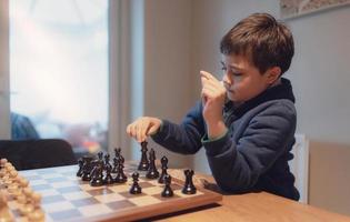 menino concentrado desenvolvendo estratégia de xadrez, jogando jogo de tabuleiro com amigo ou família em casa. atividade ou hobby para o conceito de família foto