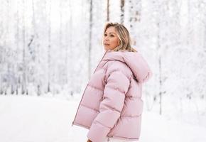 jovem loira em roupas de inverno andando na floresta de inverno nevado foto