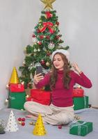 feliz natal e boas festas uma jovem com um rosto bonito em uma camisa vermelha mostra alegria com caixas de presente em uma casa com uma árvore de natal decorada com uma árvore de natal. retrato antes do natal foto