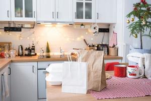 recipientes de serviço de entrega de comida na mesa branca scandi cozinha festiva na decoração de natal. véspera de ano novo, economizando tempo, com preguiça de cozinhar, pedido quente, caixa de plástico descartável à luz das fadas. brincar foto