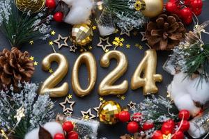as figuras douradas 2024 feitas de velas em um fundo de ardósia de pedra preta são decoradas com uma decoração festiva de estrelas, lantejoulas, ramos de abeto, bolas e guirlandas. cartão, feliz ano novo.