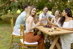 grupo de jovens felizes torcendo com limonada fresca e comendo frutas no jardim foto