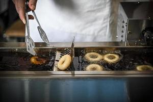 a mão de uma mulher no processo de fritar pequenos donuts no óleo profundo foto