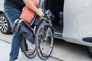 mulher asiática, dobrar e levantar a cadeira de rodas para o carro dela. conceito de acessibilidade. foto