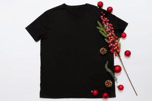 feche a camiseta modelo em branco preto com espaço de cópia e o conceito de férias de natal. t-shirt de maquete de vista superior e decorações vermelhas de feriados em fundo branco. feliz ano novo acessórios. roupa de natal foto