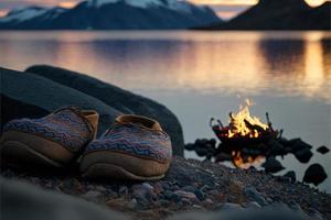 um par de chinelos aconchegantes, aninhados no deserto da noruega. a luz dourada da fogueira ilumina os chinelos, dando-lhes uma aparência acolhedora e convidativa. casa confortos ao ar livre. foto
