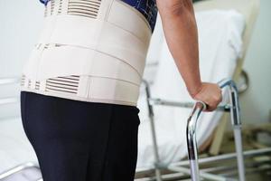 dor sênior asiática nas costas usando cinto de suporte elástico com andador. foto