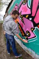 um jovem com um capuz cinza pinta graffiti em rosa e verde c foto