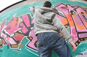 um jovem com um capuz cinza pinta graffiti em rosa e verde c foto