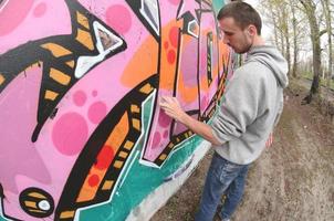 um jovem com um capuz cinza pinta graffiti em rosa e verde c foto