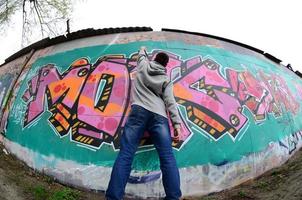 um jovem com um capuz cinza pinta graffiti em rosa e verde c foto