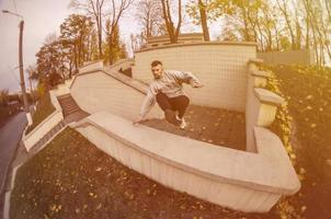 um jovem dá um salto pelo parapeito de concreto. o atleta pratica parkour, treinando em condições de rua. o conceito de subculturas esportivas entre os jovens foto