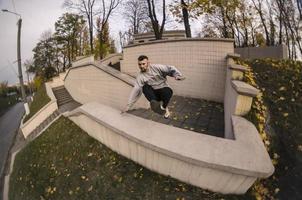 um jovem dá um salto pelo parapeito de concreto. o atleta pratica parkour, treinando em condições de rua. o conceito de subculturas esportivas entre os jovens foto