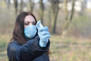 jovem com máscara protetora mostra frascos de spray desinfetante ao ar livre em madeira de primavera foto