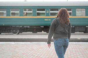 uma jovem ruiva está de pé na plataforma ferroviária e observando o trem que parte. a mulher estava atrasada para o trem. vista traseira foto